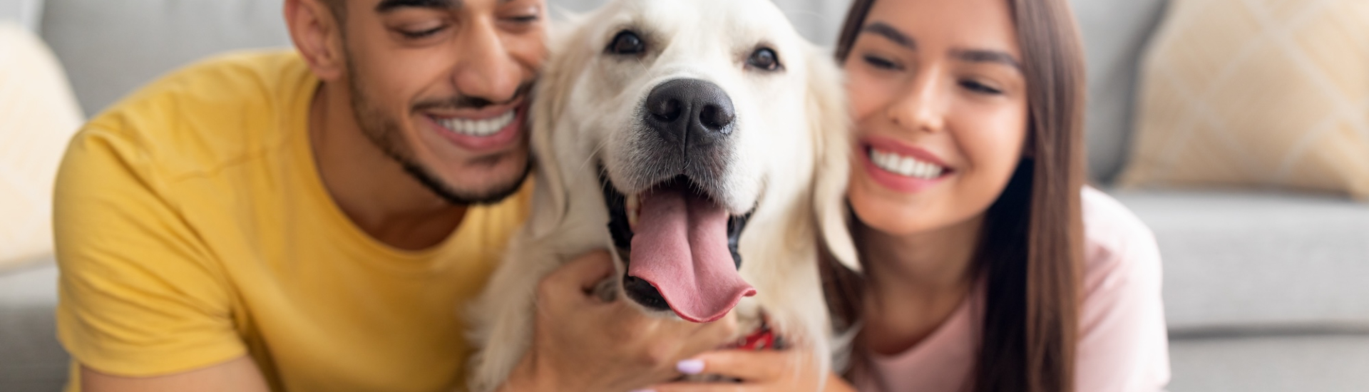 Portrait of happy multiracial couple hugging adorable dog, cuddling with their pet at home.